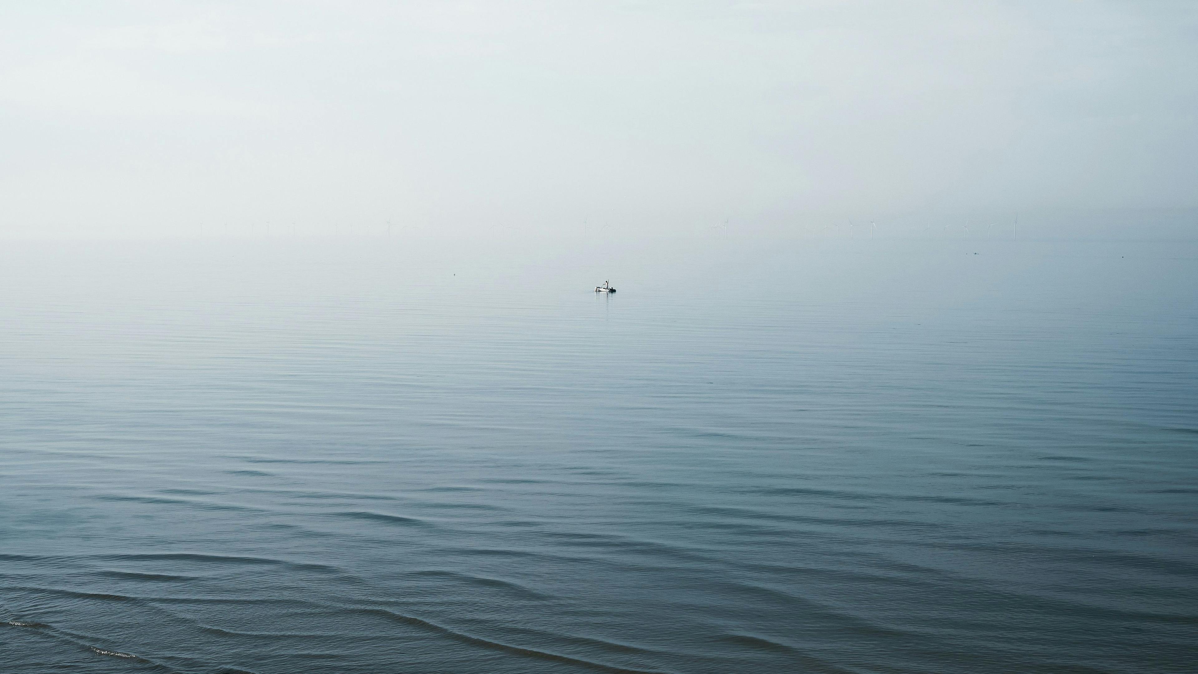 A lone boat disappearing into the haze of blue sea